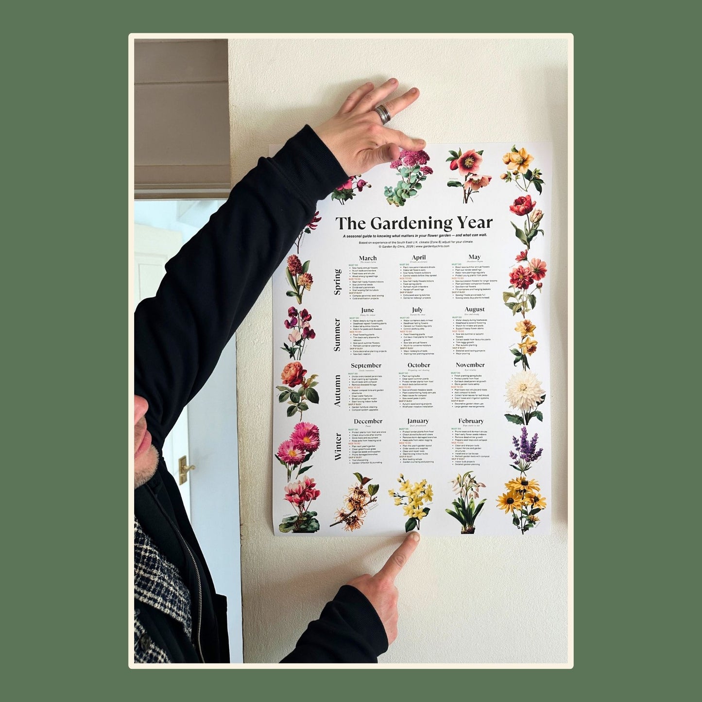 A man holding up The Gardening Year Poster on a wall.